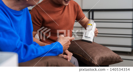 Asian son helping senior father with home cleaning using lint remover. Asian son helping senior father with home cleaning using lint remover. 140534354