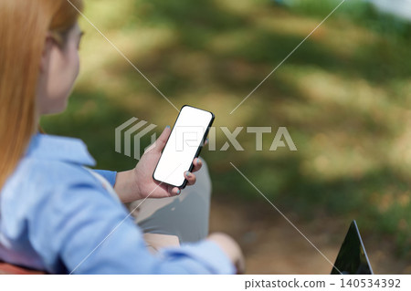 Asian woman holding smartphone with blank screen in outdoor park Asian woman holding smartphone with blank screen in outdoor park 140534392
