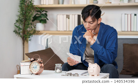 Asian man reviewing bills for budgeting, personal finance planning at home Asian man reviewing bills for budgeting, personal finance planning at home 140534396