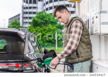 Young man refueling black car at urban gas station on rainy day in Germany Young man refueling black car at urban gas station on rainy day in Germany 140534427