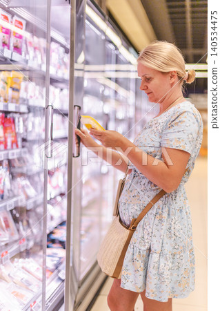 Woman reading food label while choosing products from refrigerated supermarket section, grocery shopping in modern retail store Woman reading food label while choosing products from refrigerated supermarket section, grocery shopping in modern retail store 140534475