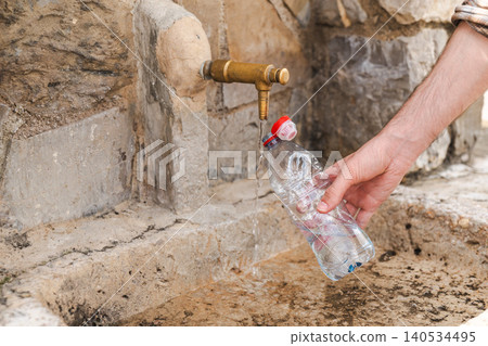 Refilling reusable water bottle from public drinking fountain in mountain village 140534495