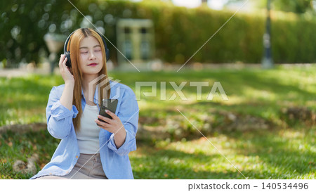Asian woman listening to music with headphones and smartphone in park 140534496