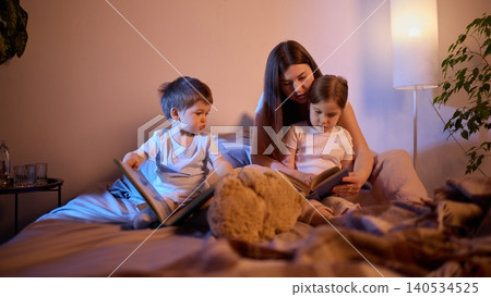 Mother reading books with children on bed in warm evening light Mother reading books with children on bed in warm evening light 140534525
