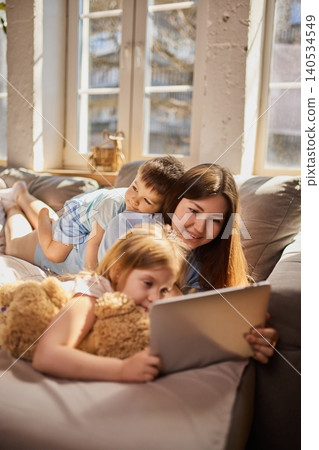 Mother with children using tablet together on sofa in bright living room. Mother with children using tablet together on sofa in bright living room. 140534549
