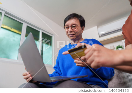 East Asian man helping senior man with online shopping using laptop and credit card East Asian man helping senior man with online shopping using laptop and credit card 140534553