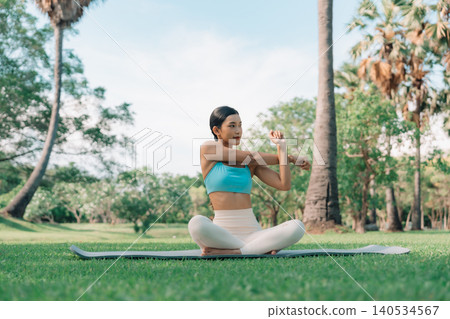 Asian woman practicing seated side stretch yoga pose outdoors in a peaceful park Asian woman practicing seated side stretch yoga pose outdoors in a peaceful park 140534567