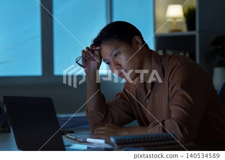 Asian man experiencing overwork and stress working late night at home office 140534589