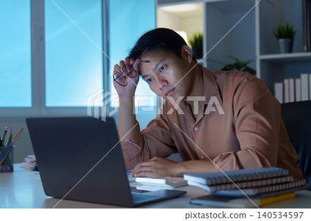 Asian man working late at home office, feeling stress and overwork Asian man working late at home office, feeling stress and overwork 140534597