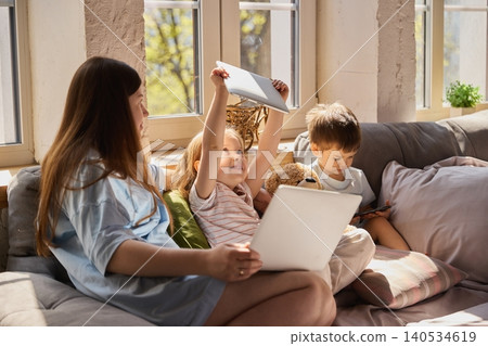 Mother with children using laptop and tablet together on sofa in bright living room. 140534619