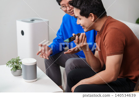 Asian senior and young man using smart home voice assistant at home 140534639
