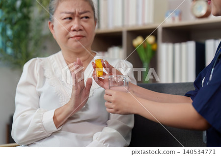 Senior woman refusing medication offered by caregiver Senior woman refusing medication offered by caregiver 140534771