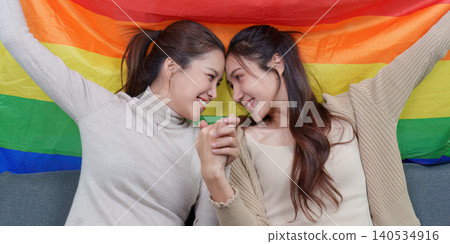 Asian lesbian couple holding hands, intimate moment with rainbow pride flag Asian lesbian couple holding hands, intimate moment with rainbow pride flag 140534916
