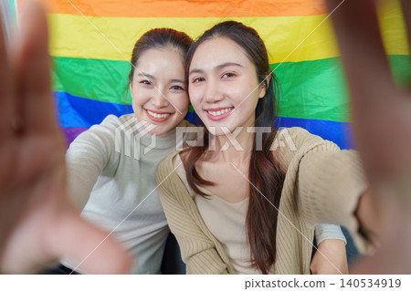 Happy Asian LGBTQ couple smiling, embracing in front of pride flag, diversity Happy Asian LGBTQ couple smiling, embracing in front of pride flag, diversity 140534919