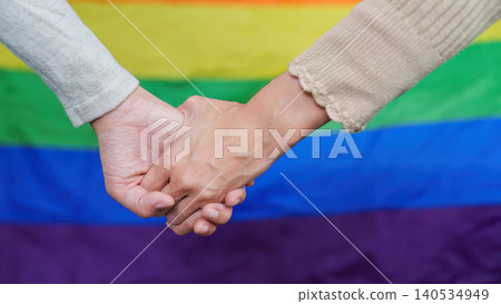 LGBTQ women couple holding hands in front of rainbow pride flag LGBTQ women couple holding hands in front of rainbow pride flag 140534949