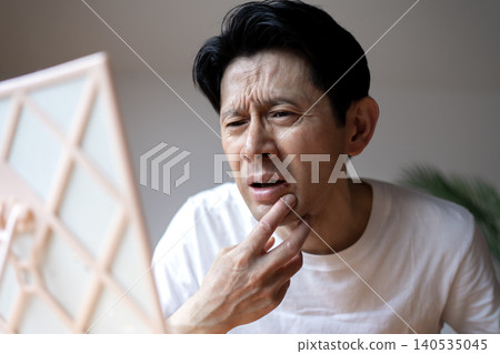 A middle-aged man grimaces, looking in the mirror and troubled by the symptoms of a cold sore on his lip. A middle-aged man grimaces, looking in the mirror and troubled by the symptoms of a cold sore on his lip. 140535045