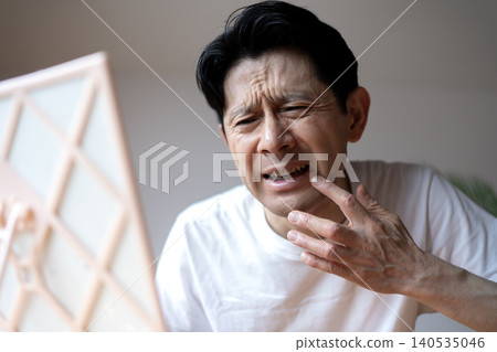 A middle-aged man grimaces, looking in the mirror and troubled by the symptoms of a cold sore on his lip. A middle-aged man grimaces, looking in the mirror and troubled by the symptoms of a cold sore on his lip. 140535046