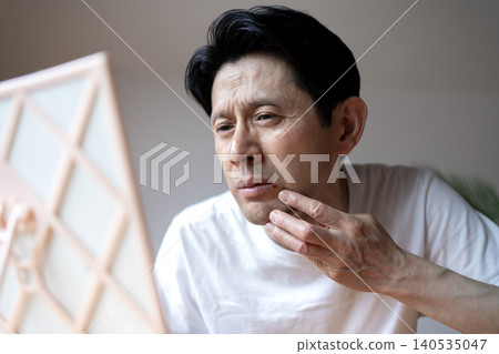 A middle-aged man grimaces, looking in the mirror and troubled by the symptoms of a cold sore on his lip. A middle-aged man grimaces, looking in the mirror and troubled by the symptoms of a cold sore on his lip. 140535047