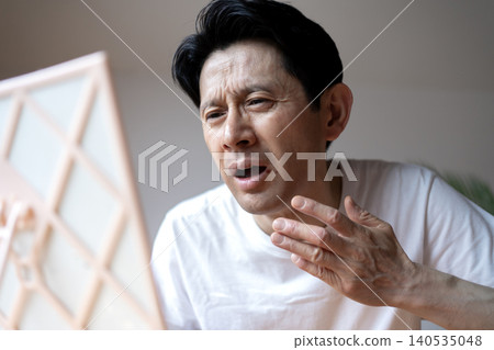 A middle-aged man grimaces, looking in the mirror and troubled by the symptoms of a cold sore on his lip. A middle-aged man grimaces, looking in the mirror and troubled by the symptoms of a cold sore on his lip. 140535048