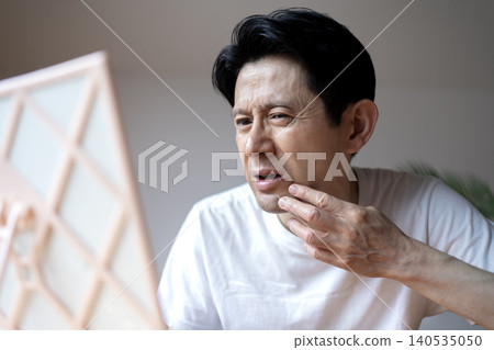 A middle-aged man grimaces, looking in the mirror and troubled by the symptoms of a cold sore on his lip. A middle-aged man grimaces, looking in the mirror and troubled by the symptoms of a cold sore on his lip. 140535050
