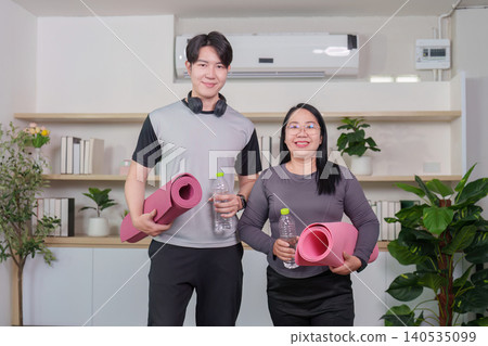 Asian couple holding yoga mats and water bottles after home workout Asian couple holding yoga mats and water bottles after home workout 140535099