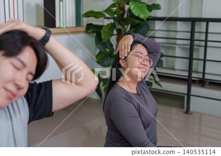 Asian plus-size woman stretching neck during home workout for flexibility Asian plus-size woman stretching neck during home workout for flexibility 140535114