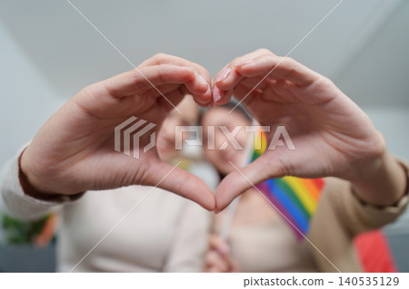 Asian LGBTQ couple making heart shape with hands, rainbow pride flag Asian LGBTQ couple making heart shape with hands, rainbow pride flag 140535129