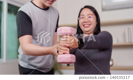 Asian man assisting plus-size woman with dumbbell exercise at home Asian man assisting plus-size woman with dumbbell exercise at home 140535217