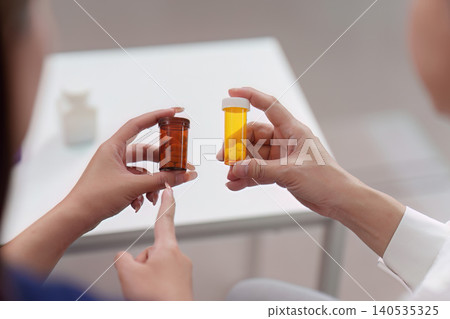 Doctor and patient comparing different medication pill bottles for treatment Doctor and patient comparing different medication pill bottles for treatment 140535325