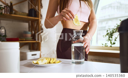 Woman adding lemon slice into water for healthy lifestyle routine. Woman adding lemon slice into water for healthy lifestyle routine. 140535360