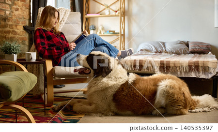 Woman reading with saint bernard dog at home comfortable pet friendly lifestyle Woman reading with saint bernard dog at home comfortable pet friendly lifestyle 140535397