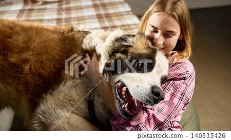 Woman hugging large fluffy dog sitting together indoors in cozy home. Woman hugging large fluffy dog sitting together indoors in cozy home. 140535426