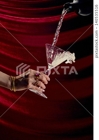 Dramatic splash of champagne overflowing martini glass on red velvet background high speed luxury drink concept Dramatic splash of champagne overflowing martini glass on red velvet background high speed luxury drink concept 140535516