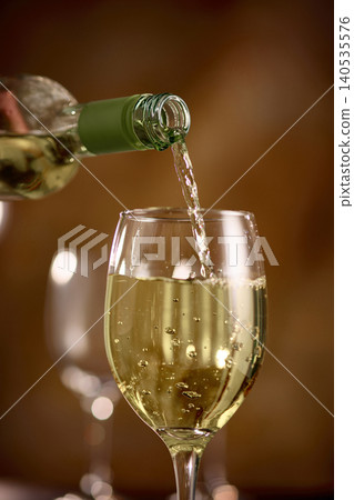 Close up white wine pouring into glass with bubbles in elegant warm light Close up white wine pouring into glass with bubbles in elegant warm light 140535576