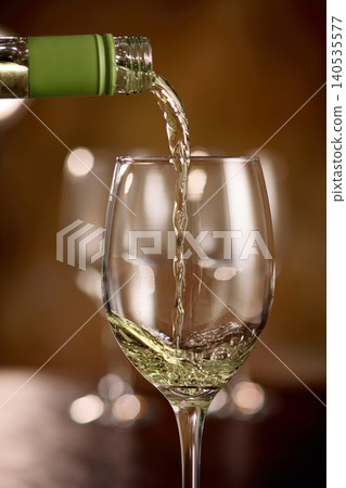 White wine pouring into glass with soft bokeh background in warm restaurant light White wine pouring into glass with soft bokeh background in warm restaurant light 140535577