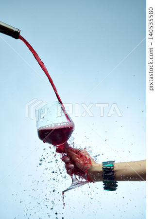 Close up red wine stream filling glass with splashes isolated on blue background Close up red wine stream filling glass with splashes isolated on blue background 140535580