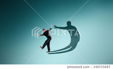 Man balancing with oversized shadow reaching forward symbolizing fear and inner pressure Man balancing with oversized shadow reaching forward symbolizing fear and inner pressure 140535697
