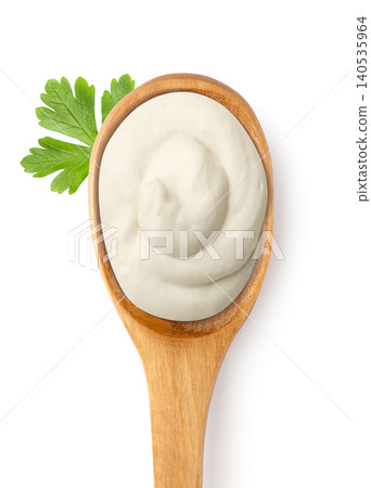 Sour cream in a wooden spoon with a parsley leaf on a white. Top view Sour cream in a wooden spoon with a parsley leaf on a white. Top view 140535964