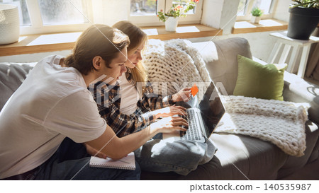 Couple completing online purchase together on laptop in sunlit living room. Couple completing online purchase together on laptop in sunlit living room. 140535987
