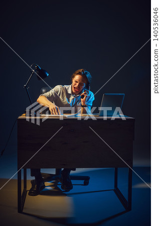 Man shouting on phone while working at desk in dramatic studio lighting. Man shouting on phone while working at desk in dramatic studio lighting. 140536046