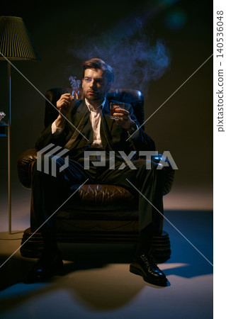 Confident man in suit smoking cigar and holding whiskey in dramatic low key lighting. 140536048