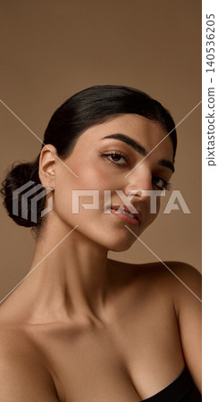 Close beauty portrait of woman with glossy skin and sleek bun on brown background. Close beauty portrait of woman with glossy skin and sleek bun on brown background. 140536205