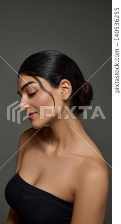 Elegant side portrait of woman with sleek bun and glowing skin on gray background. Elegant side portrait of woman with sleek bun and glowing skin on gray background. 140536255