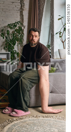 Tired man with oversized arm sits on sofa in cozy apartment. Tired man with oversized arm sits on sofa in cozy apartment. 140536350