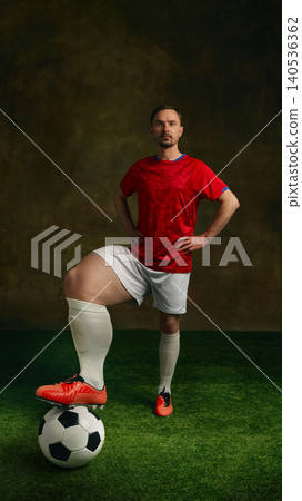 Soccer player with oversized leg stands on ball in dramatic sports portrait. Soccer player with oversized leg stands on ball in dramatic sports portrait. 140536362