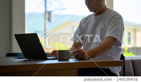 一個男人一邊用筆記型電腦工作,一邊喝咖啡。 一個男人一邊用筆記型電腦工作,一邊喝咖啡。 140536458