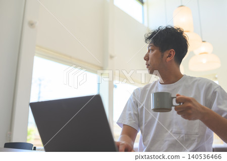 A man looking at his PC with a cup of coffee in his hand. A man looking at his PC with a cup of coffee in his hand. 140536466