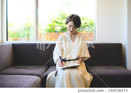 A woman writing on a clipboard by the window. A woman writing on a clipboard by the window. 140536475