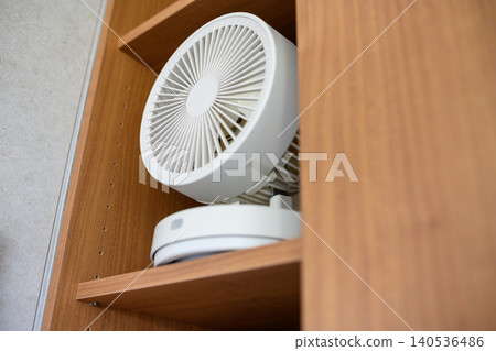 White tabletop fan on a wooden shelf White tabletop fan on a wooden shelf 140536486