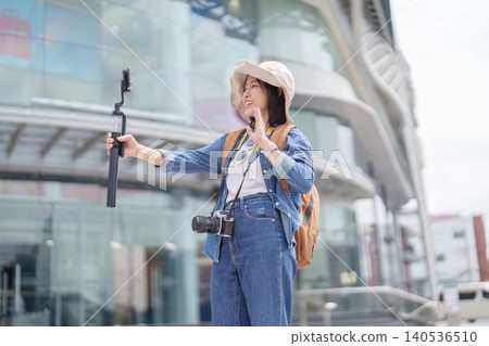 Happy Asian woman vlogging with smartphone and gimbal in city for summer travel content creation Happy Asian woman vlogging with smartphone and gimbal in city for summer travel content creation 140536510